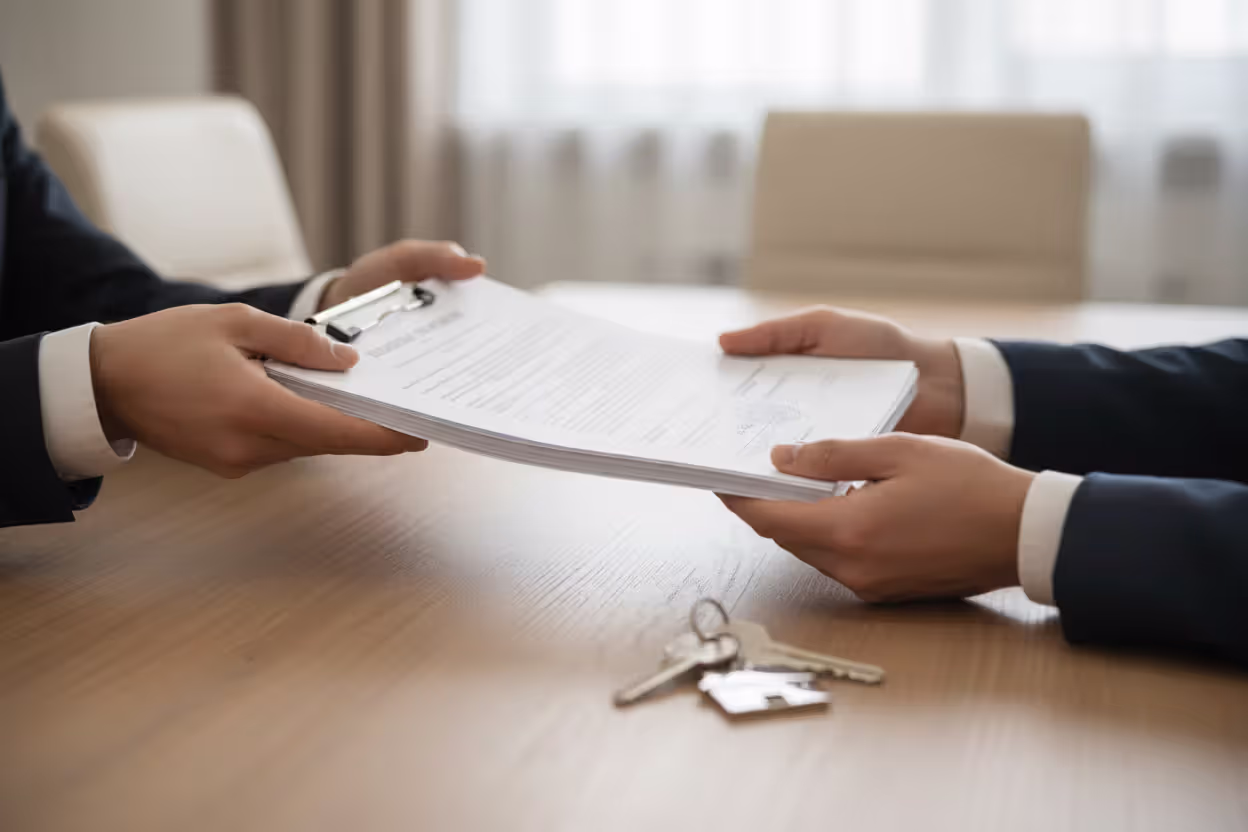 Hands exchanging official mortgage documents with house keys on a desk during closing process